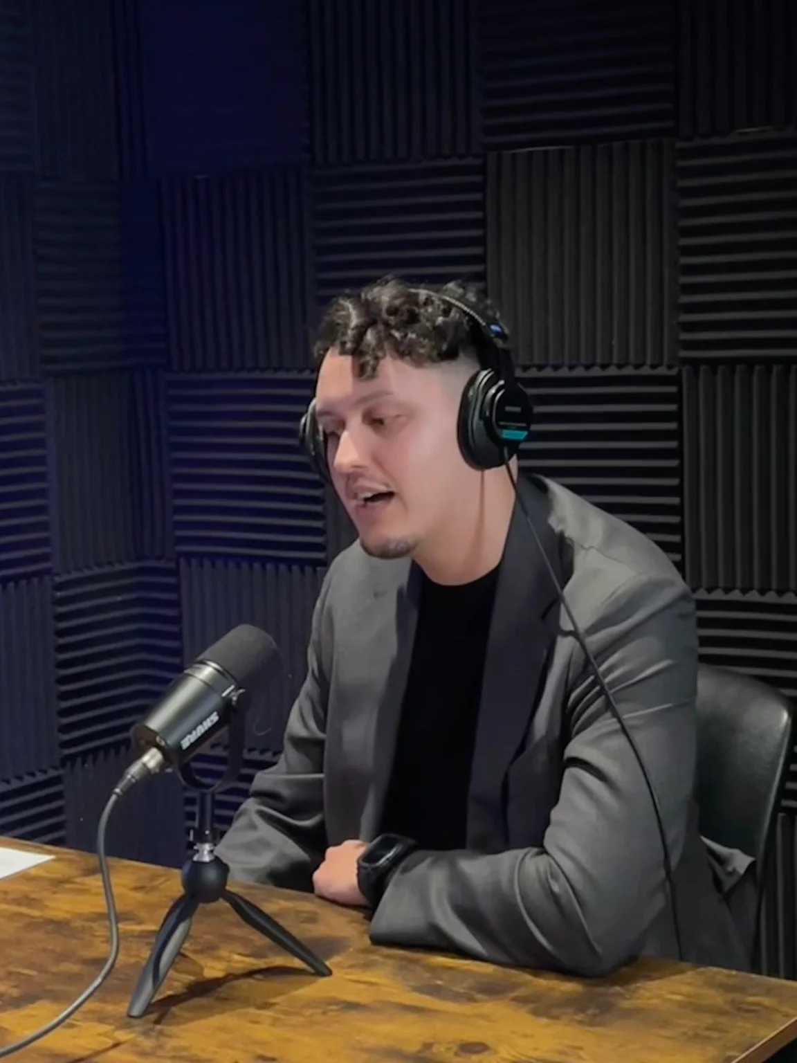 Julian Badillo wearing headphones and speaking into a microphone during a podcast recording